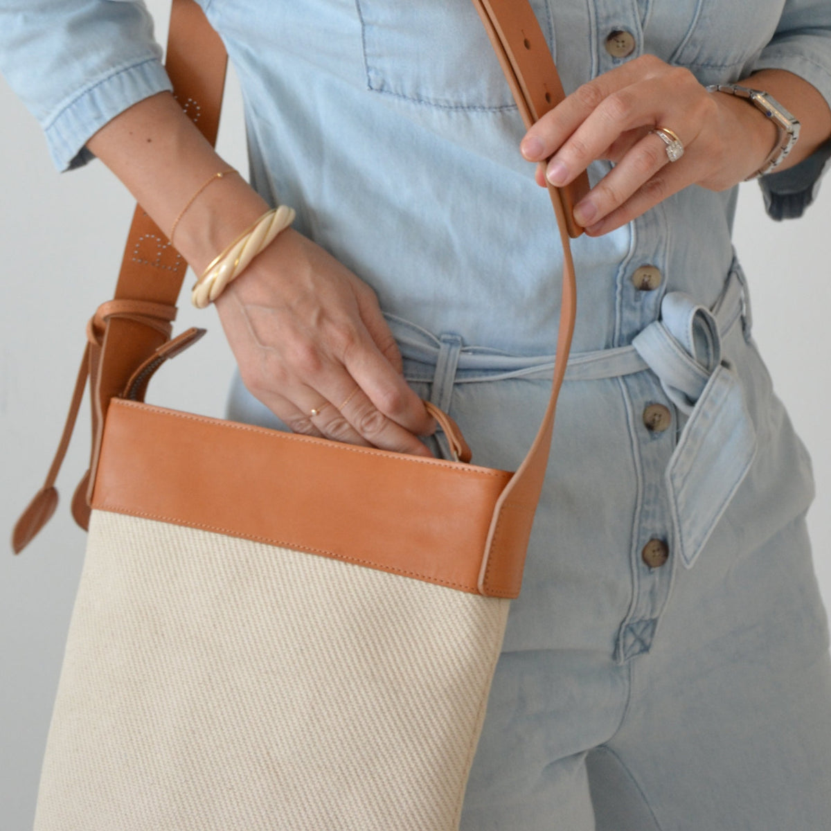 Person holding a beige tote bag with a brown leather strap against a plain background